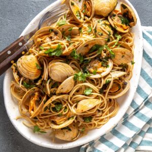 Clams spaghetti on white plate with white wine, gray background. Top view