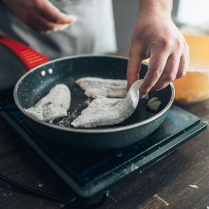 Chef cooking sea bass fish fillet on a frying pan