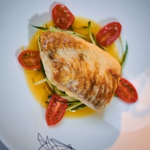 Fillet of grilled and baked codfish served with vegetables and oil sauce, on a dish in a restaurant