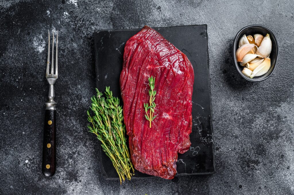 Venison raw steak from wild meat. Black background. Top view